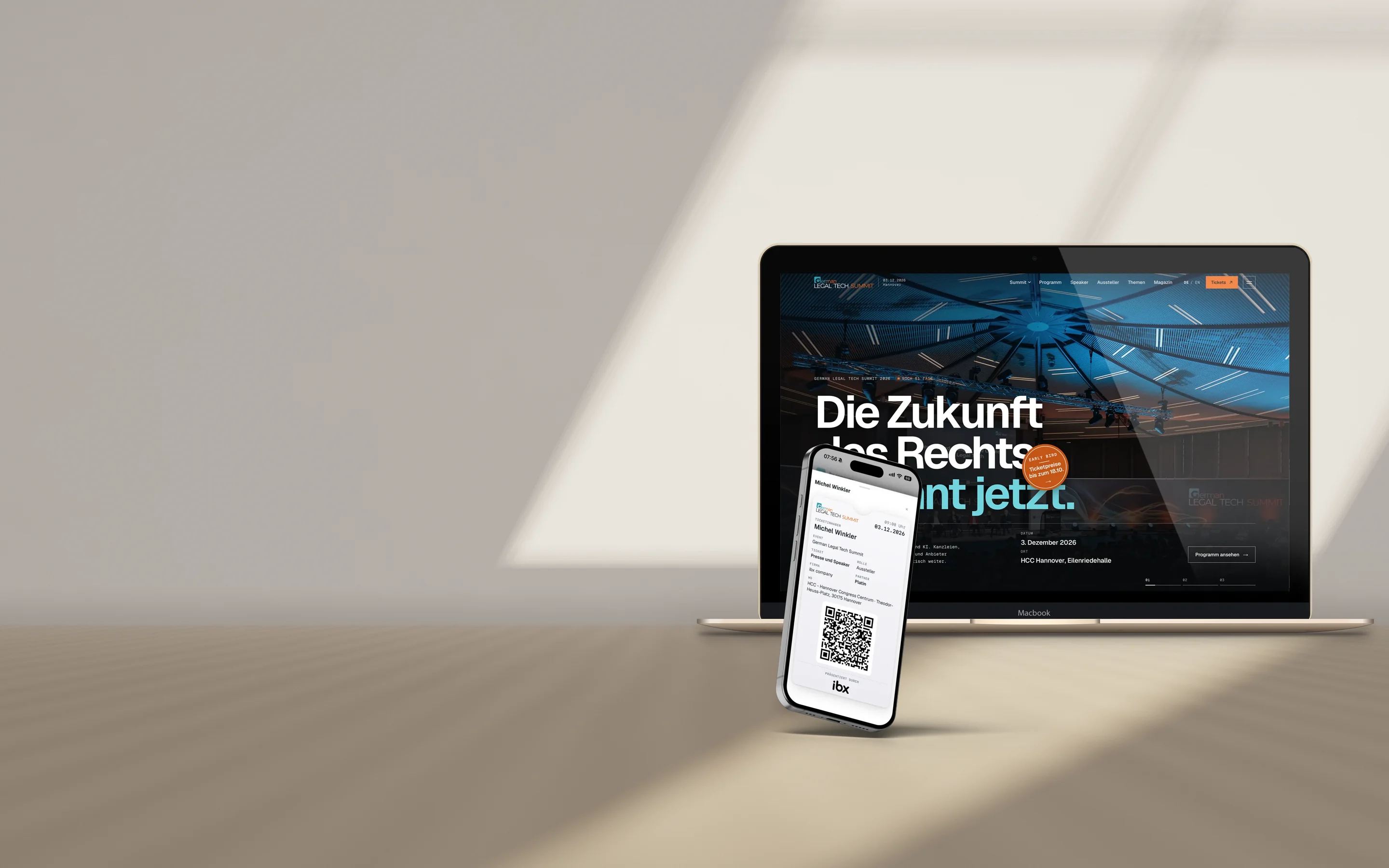 MacBook und iPhone auf einem Eichentisch: auf dem MacBook die Startseite des German Legal Tech Summit, auf dem iPhone ein digitales Ticket für den Kongress.