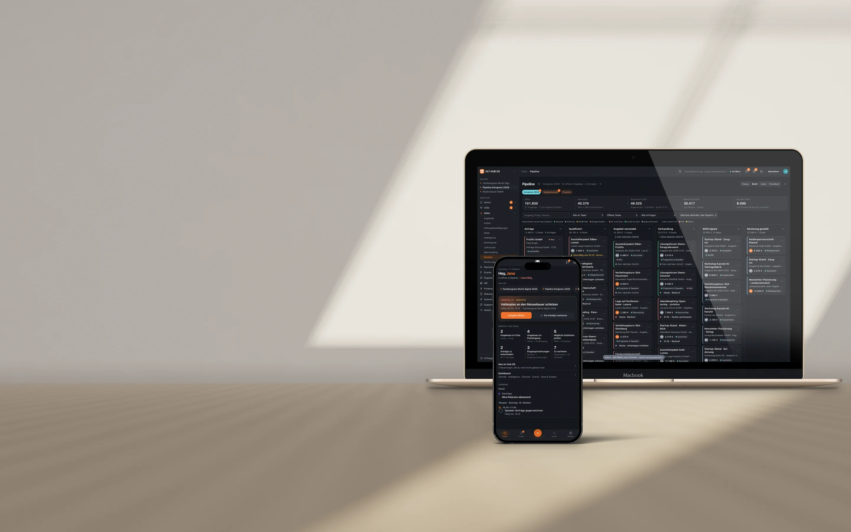 MacBook und iPhone auf einem Eichentisch mit dem Hub OS des German Legal Tech Hub: auf dem MacBook die Vertriebspipeline, auf dem iPhone die Startseite mit offenen Aufgaben. Demo mit erfundenen Daten.