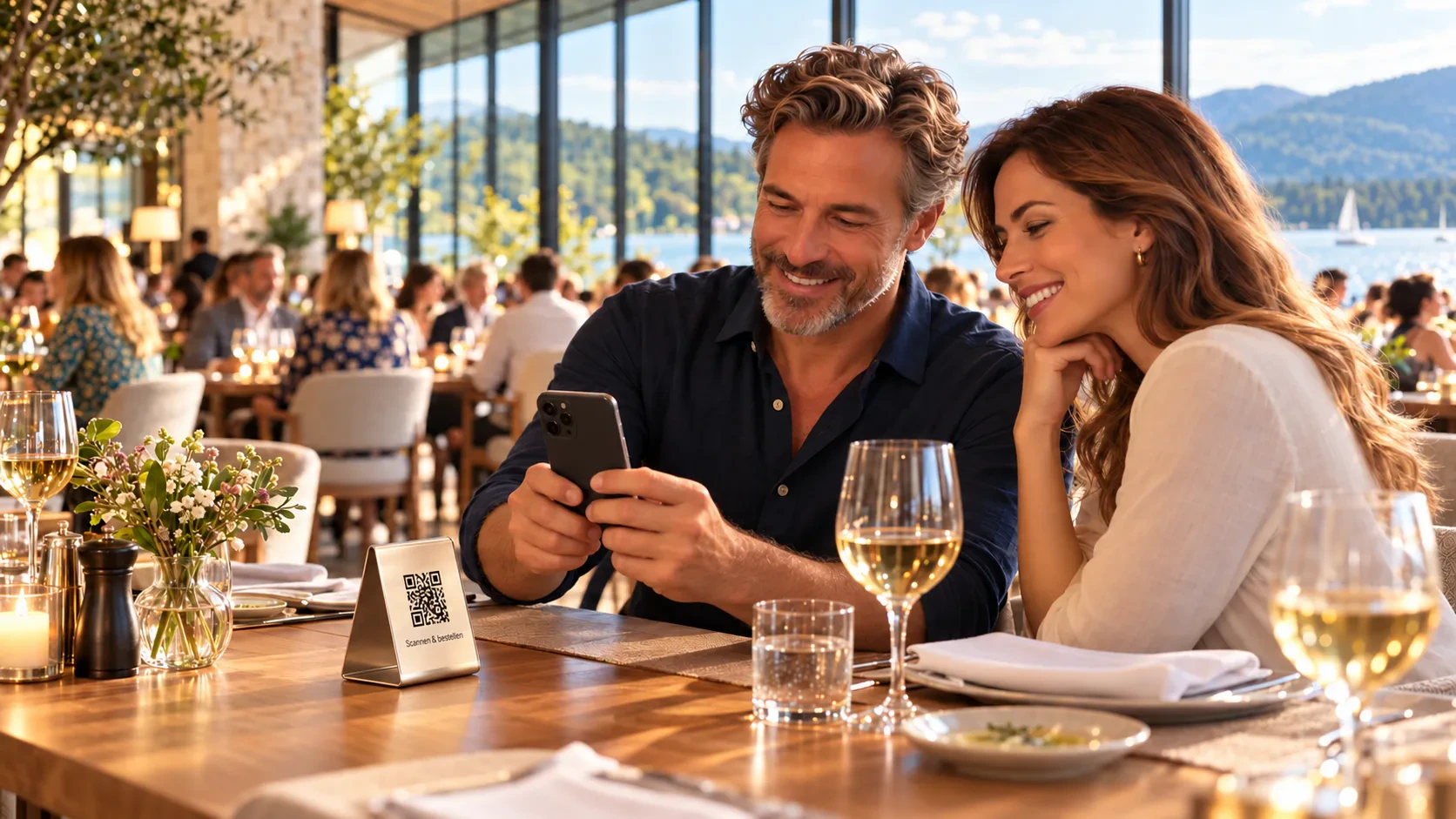 Symbolbild: Ein Paar sitzt im Restaurant mit Blick auf den See und bestellt über das Smartphone, auf dem Tisch steht ein Aufsteller mit QR Code.